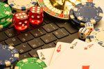 Photo of laptop keyboard covered with casino game pieces including cards, dice, chips and roulette