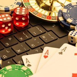 Photo of laptop keyboard covered with casino game pieces including cards, dice, chips and roulette
