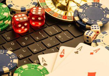 Photo of laptop keyboard covered with casino game pieces including cards, dice, chips and roulette