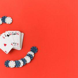 Red background, playing cards and poker chips placed to the left to illustration a story titled The Types of Card Games You Will Find in Casinos