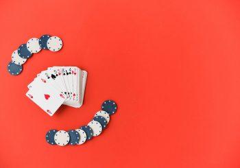 Red background, playing cards and poker chips placed to the left to illustration a story titled The Types of Card Games You Will Find in Casinos